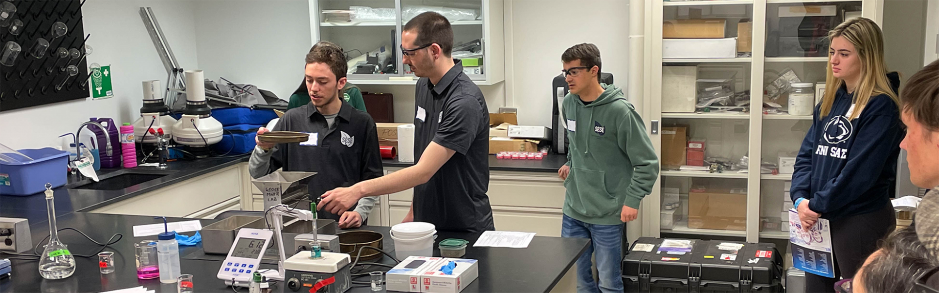 2 male students doing an experiment while other students watch